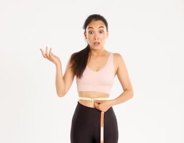 Perempuan sedang mengukur berat badan menggunakan meteran tali