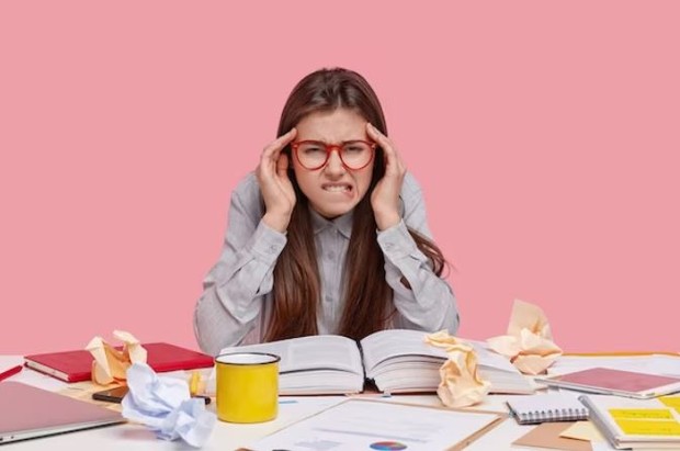 Perempuan sedang memegang kepalanya terlihat sulit konsentrasi