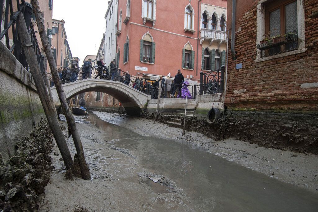Passengers get off a gondola docked along a canal during a low tide in Venice, Italy, Tuesday, Feb. 21, 2023. Some of Venice's secondary canals have practically dried up lately due a prolonged spell of low tides linked to a lingering high-pressure weather system. (AP Photo/Luigi Costantini)