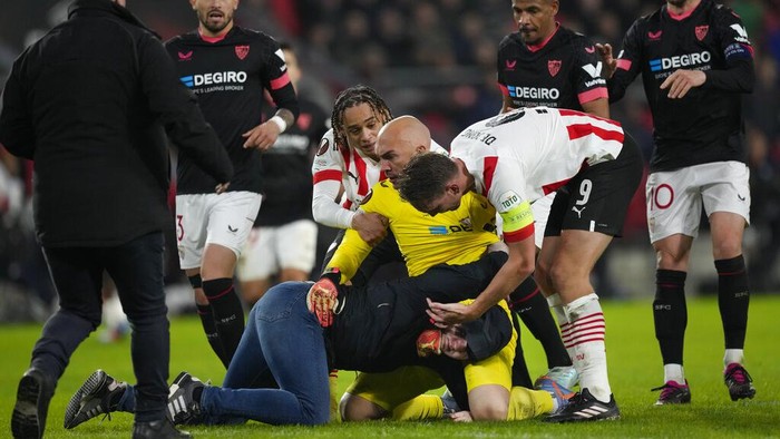 Marko Dmitrovic vs Penyusup Lapangan Players intervene after a PSV fan, on the pitch, attacked Sevilla's goalkeeper Marko Dmitrovic, in yellow, during the Europa League playoff second leg soccer match between PSV and Sevilla at the Philips stadium in Eindhoven, Netherlands, Thursday, Feb. 23, 2023. (AP Photo/Peter Dejong)