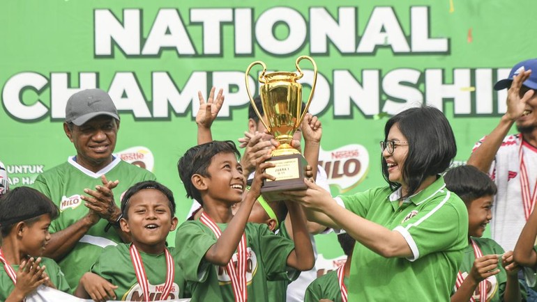 Business Executive Officer Beverages Business Unit PT Nestle Indonesia Mirna Tri Handayani? (kanan) disaksikan Legenda Sepak Bola Indonesia Rully Rudolf Nere (kiri) menyerahkan piala kepada pemain SSB Asybar Rembang usai memenangkan Milo National Championship ketegori U-11 di Stadion Gelanggang Mahasiswa Soemantri Brodjonegoro, Jakarta. 