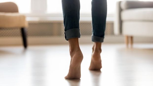 Rear view close up cropped image caucasian barefoot woman feet in blue jeans, female stands on tiptoes enjoys modern home warm electric underfloor heating or active girl moving dancing indoors concept