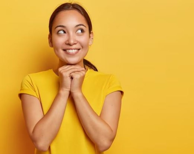 Perempuan berbaju kuning dengan wajah penuh harapan sambil tersenyum