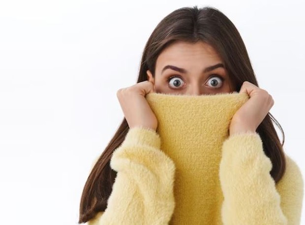 Perempuan menutupi hidung dan mulut dengan sweaternya dan mata melotot terlihat terkejut