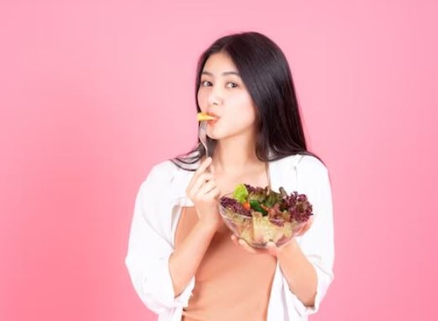A woman is eating while holding a bowl full of salad