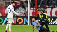 Tidak, sosok dengan rompi warna hijau stabilo tidak hendak membantu si penyusup lapangan berdiri untuk melanjutkan niat memeluk Messi. Justru sebaliknya. Foto: REUTERS/ANGELIKA WARMUTH