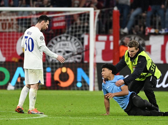 Soccer Football - Champions League - Round of 16 - Second Leg - Bayern Munich v Paris St Germain - Allianz Arena, Munich, Germany - March 8, 2023  A pitch invader is detained by a steward as Paris St Germain's Lionel Messi looks dejected after the match REUTERS/Angelika Warmuth