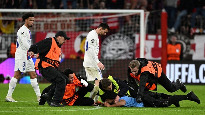 Soccer Football - Champions League - Round of 16 - Second Leg - Bayern Munich v Paris St Germain - Allianz Arena, Munich, Germany - March 8, 2023 A pitch invader is detained by stewards as Paris St Germain's Lionel Messi and Warren Zaire-Emery look dejected after the match REUTERS/Angelika Warmuth TPX IMAGES OF THE DAY