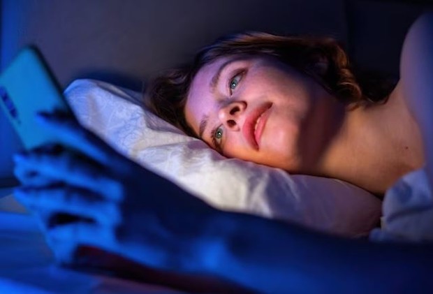 Perempuan sedang main handphone sambil tiduran dan gelap