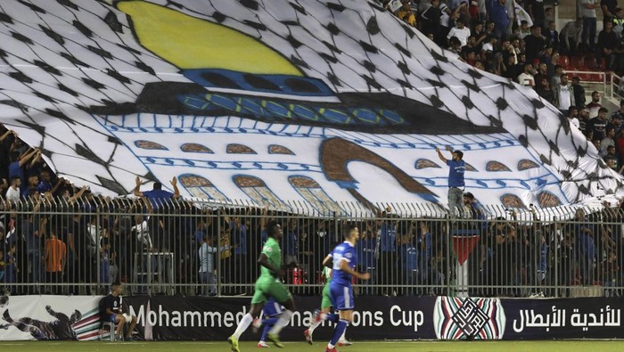 Spectators hold a huge flag depicting Jerusalems Dome of the Rock mosque during a match between Palestinian team Hilal al-Quds and Moroccos Raja Casablanca in the Arab Club Champions Cup at Faisal Husseini stadium in the town of al-Ram, between Jerusalem and Ramallah, on October 3, 2019. - The first Moroccan football team were playing in the occupied Palestinian territories today, as the head of the Palestinian football association announced the Saudi national team would also visit. Arab clubs and national teams have historically refused to play in the West Bank, where the Palestinian national team plays, as it required them to apply for Israeli entry permits. (Photo by ABBAS MOMANI / AFP) (Photo by ABBAS MOMANI/AFP via Getty Images)