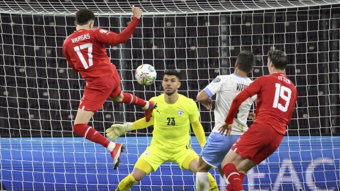 Switzerland's Ruben Vargas, left, scores past Israel's goalkeeper Omri Glazer, center, and Miguel Vitor during the Euro 2024 qualifying group I soccer match between Switzerland and Israel, at the Stade de Geneve, in Geneva, Switzerland, Tuesday, March 28, 2023. (Salvatore Di Nolfi/Keystone via AP)