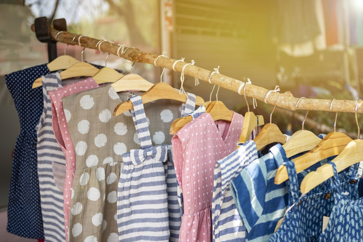 Kids's fashion, cute little girl dress hanging on wooden stick over blurred cloth shop background