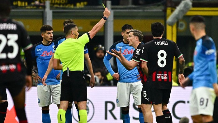 Romanian referee Istvan Kovacs (L) gives a yellow card to AC Milans Belgian forward Alexis Saelemaekers during the UEFA Champions League quarter-finals first leg football match between AC Milan and SSC Napoli on April 12, 2023 at the San Siro stadium in Milan. (Photo by GABRIEL BOUYS / AFP) (Photo by GABRIEL BOUYS/AFP via Getty Images)