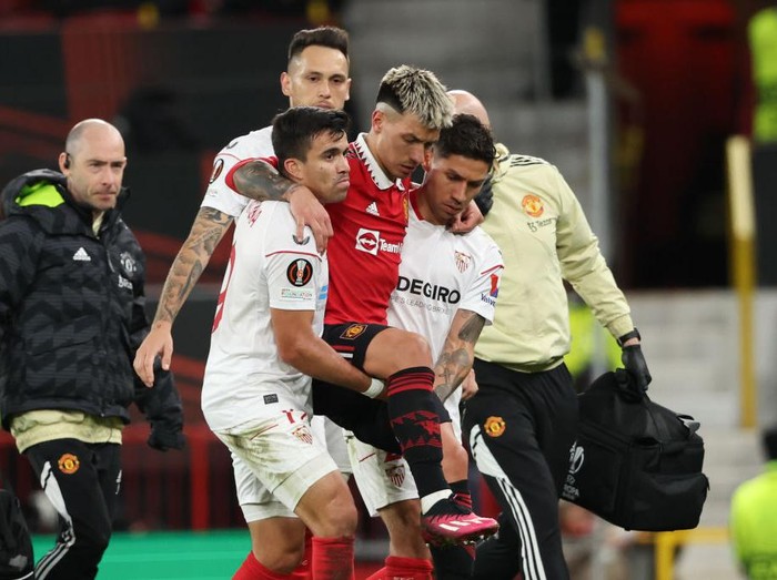 MANCHESTER, ENGLAND - APRIL 13: Marcos Acuna of Sevilla and Gonzalo Montiel of Sevilla carry off Lisandro Martinez of Manchester United after an injury during the UEFA Europa League quarterfinal first leg match between Manchester United and Sevilla FC at Old Trafford on April 13, 2023 in Manchester, United Kingdom. (Photo by Matthew Ashton - AMA/Getty Images)