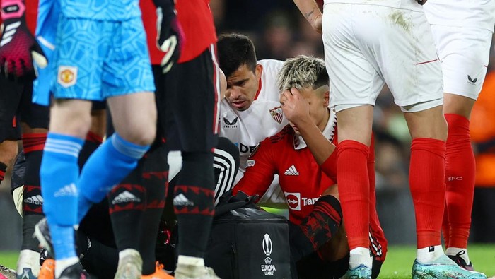 Soccer Football - Europa League - Quarter Final - First Leg - Manchester United v Sevilla - Old Trafford, Manchester, Britain - April 13, 2023  Manchester United's Lisandro Martinez receives medical attention after sustaining an injury as Sevilla's Marcos Acuna looks on Action Images via Reuters/Lee Smith