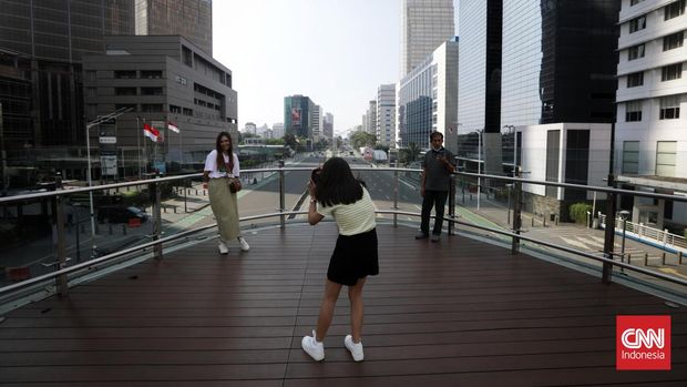 Pengunjung berfoto dan menikmati suasana kota dari anjungan Halte Transjakarta Bundaran HI, Jakarta, Jumat, 21 April 2023. Momen libur panjang lebaran Idul Fitri 1444H dimanfaatkan warga daerah liburan ke Jakarta. CNN Indonesia/Safir Makki