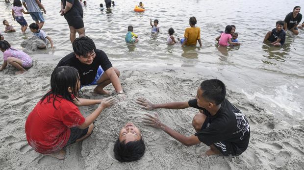 Pengunjung bermain pasir di kawasan pantai Ancol, Jakarta, Minggu (23/4/2023). Menurut data dari PT Pembangunan Jaya Ancol Tbk, pada hari kedua Idul Fitri 1444 Hijriyah jumlah kunjungan wisatawan ke objek wisata itu mencapai 97 ribu orang hingga pukul 18.00 WIB. ANTARA FOTO/M Risyal Hidayat/nym.