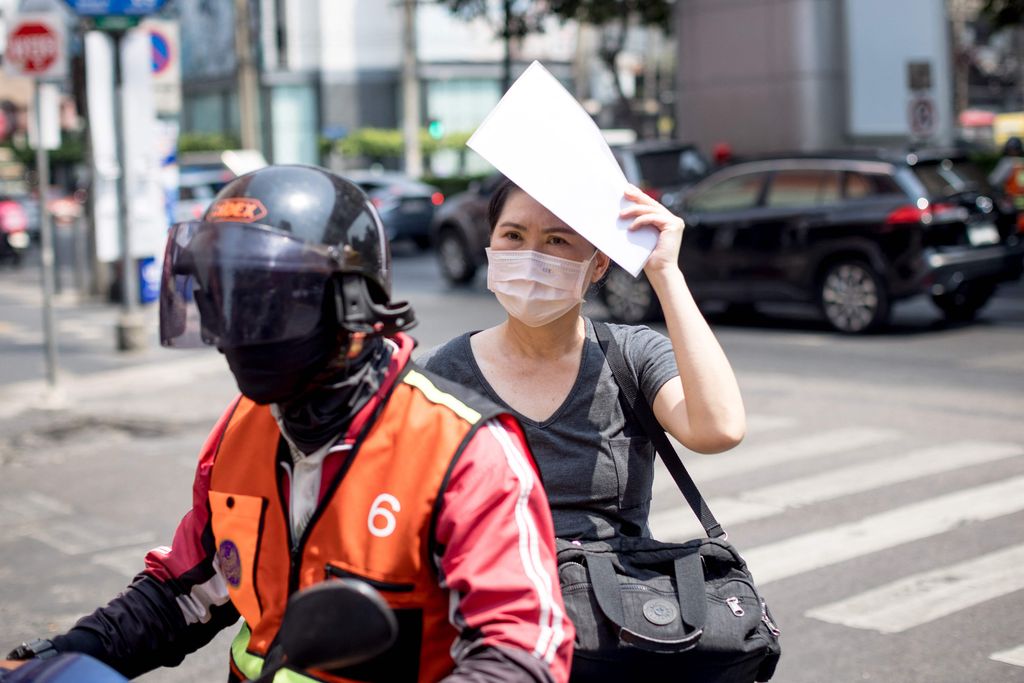 A woman riding the back of a motorbike taxi shelters herself from the sun with paper during heatwave conditions in Bangkok on April 20, 2023. - Sweltering under a blistering sun, people across South and Southeast Asia have been taking cover beneath any shelter they can find as they pray for cooling rains with record temperatures hitting the region. (Photo by Jack TAYLOR / AFP) (Photo by JACK TAYLOR/AFP via Getty Images)