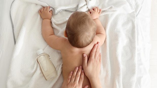 Mother massaging her baby with oil on towel after bathing, top view