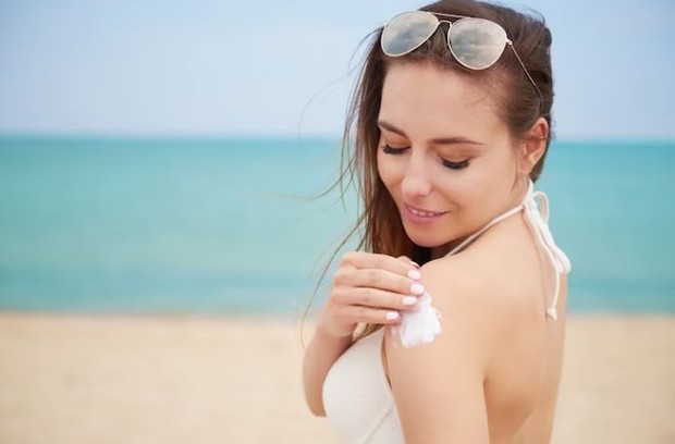 Perempuan sedang mengoleskan sunscreen di pundaknya