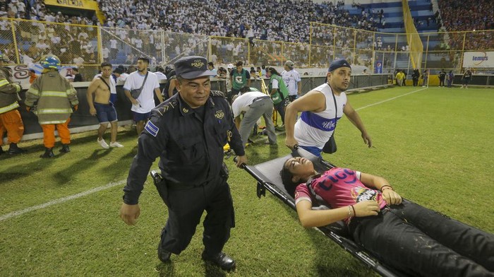 Potret Tragedi Sepakbola Mematikan di El Salvador, 12 Suporter Tewas Soccer fans are assisted by others fans at the field of the Cuscatlan stadium in San Salvador, El Salvador, Saturday, May 20, 2023. At least nine people were killed and dozens more injured when stampeding fans pushed through one of the access gates at a quarterfinal Salvadoran league soccer match between Alianza and FAS. (AP Photo/Milton Flores)