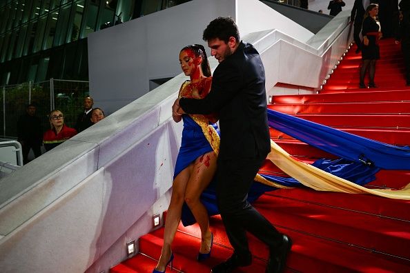 TOPSHOT - A protester, wearing a dress in the colours of the Ukrainian flag, is detained by security after she covered herself in fake blood on the stairs on the Festival Palace ahead of the screening of the film 