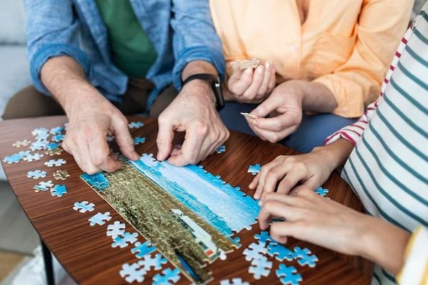 tiga orang sedang bermain puzzle bersama