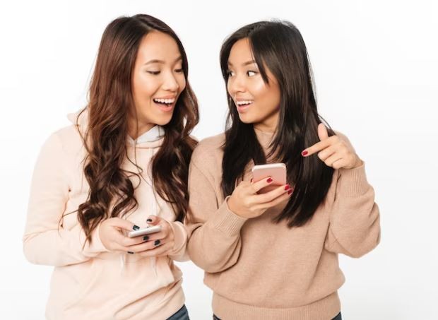 Kesukaan dan hobi/ foto: Freepik/ drobotdean Dua perempua sedang mengobrol sambil bermain ponsel