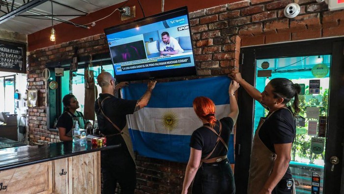 Employees of Argentinian restaurant Fiorito hang a flag while watching statements by Lionel Messi on television, in Miami, Florida, on June 7, 2023. Lionel Messi on Wednesday announced he will sign for Major League Soccer side Inter Miami, choosing the United States as his next destination over a Barcelona reunion or blockbuster deal to play in Saudi Arabia. (Photo by Giorgio Viera / AFP) (Photo by GIORGIO VIERA/AFP via Getty Images)
