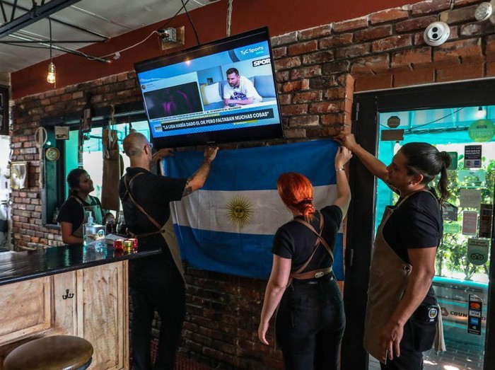 Employees of Argentinian restaurant Fiorito hang a flag while watching statements by Lionel Messi on television, in Miami, Florida, on June 7, 2023. Lionel Messi on Wednesday announced he will sign for Major League Soccer side Inter Miami, choosing the United States as his next destination over a Barcelona reunion or blockbuster deal to play in Saudi Arabia. (Photo by Giorgio Viera / AFP) (Photo by GIORGIO VIERA/AFP via Getty Images)
