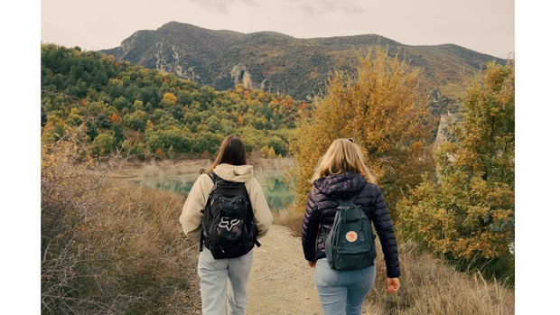 Ilustrasi dua orang perempuan yang terlihat sedang traveling di alam terbuka.