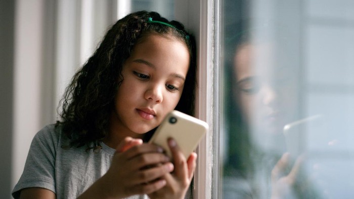 Window, ponsel cerdas and girl on social media, connection and search internet in house. Young female, kid and child with phone, online reading or communication being calm, playing games, device or chat