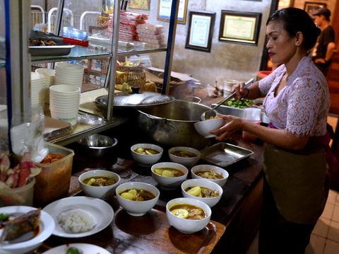 Pramusaji mengantarkan sajian kuliner ikan laut untuk pembeli di Warung Mak Beng, Sanur, Denpasar, Bali, Kamis (29/6/2023). Warung yang telah berdiri sejak tahun 1941 dengan menjual ikan laut goreng, sup kepala ikan laut , dan sup sayur tersebut masuk dalam daftar restoran paling legendaris nomor tiga di dunia versi TasteAtlas. ANTARA FOTO/Fikri Yusuf