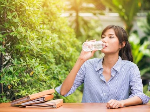 Perempuan sedang minum air putih sambill duduk