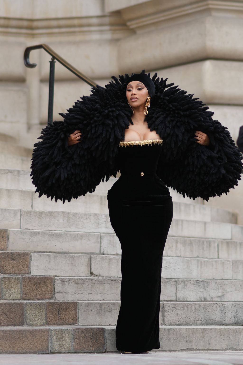 PARIS, FRANCE - JULY 03: Cardi B wears  a black velvet scarf as a hat from Schiaparelli, gold large ears and white pearls pendant earrings from Schiaparelli, a black velvet with embroidered gold metallic shoulder-off borders / long tube dress from Schiaparelli, gold large bracelets from Schiaparelli, pumps heels shoes , a black fluffy oversized puffy jacket from Schiaparelli, outside Schiaparelli, during the Haute Couture Fall/Winter 2023/2024 as part of  Paris Fashion Week on July 03, 2023 in Paris, France. (Photo by Edward Berthelot/Getty Images)