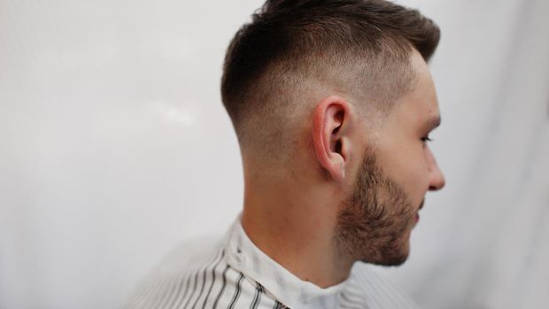 Close up head of young bearded man getting haircut at barbershop. Barber soul.