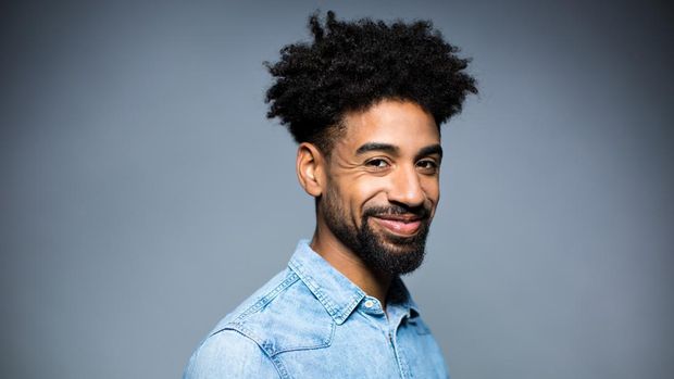 Portrait of smiling young man. Happy male is having black curly hair. He is against gray background.