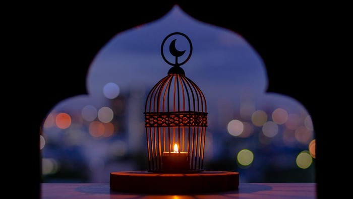 Lantern that have moon symbol on top with city bokeh light and blurred focus of paper cut for mosque shape background. Islamic new year concept.