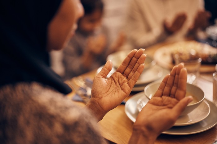 ilustrasi doa makan/buka puasa Close-up of religious Muslim woman and her family praying before the meal at dining table on Ramadan.