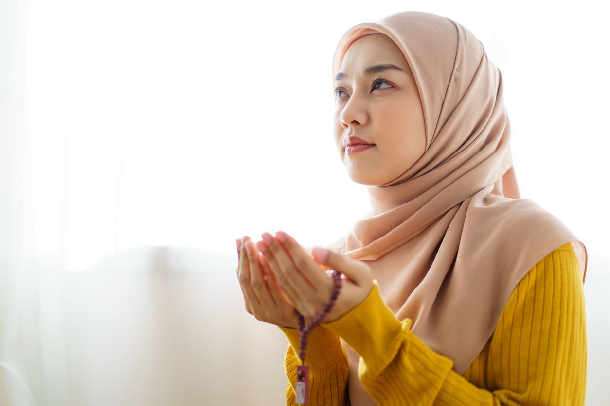 Beautiful Asian young Muslim woman sit on the floor in her house and praying for a holy god - Allah in Islam believe.
