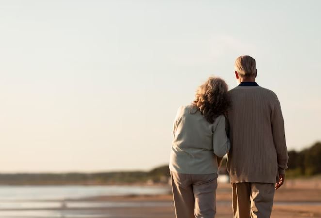 Kakek dan nenek sedang berjalan di pantai membelakangi kamera