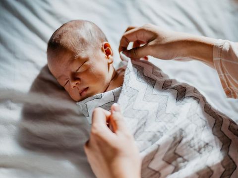 Image of an Asian mother swaddle her newborn baby on bed. Woman taking care of her sleeping baby in bedroom