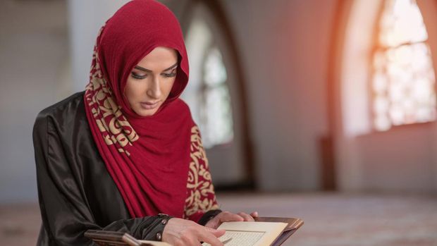 Muslim Woman Reading Koran Or Quran Wearing Traditional Dress At The Mosque.