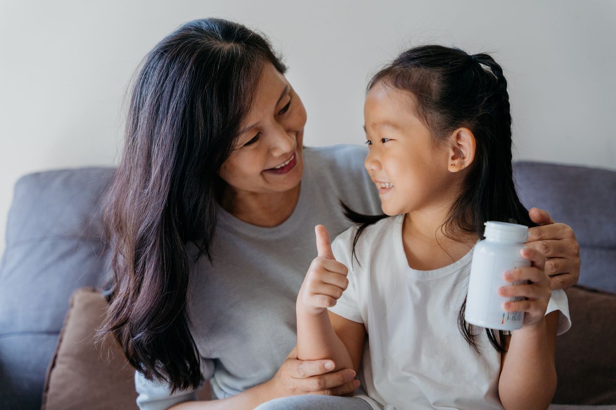 Image of a young asian girl ready to give supplement to her grandmother in living room. The supplement is good for her grandmother's health.