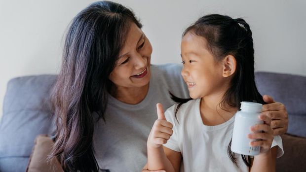 Image of a young asian girl ready to give supplement to her grandmother in living room. The supplement is good for her grandmother's health.