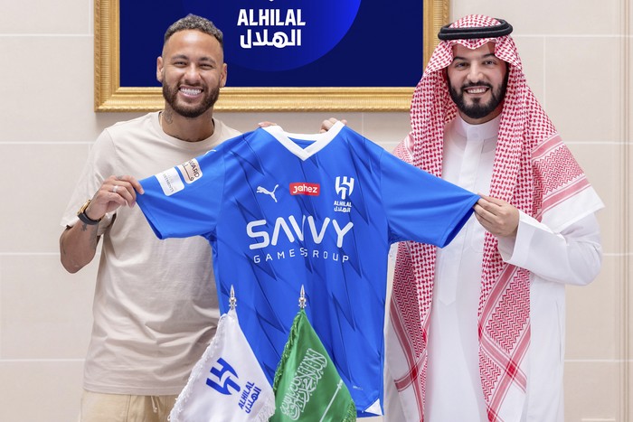 In this photo provided Al Hilal club media center, Neymar holds a Al Hilal shirt after signing with Chairman of the Board of Directors of Al Hilal, Fahad Bin Saad Bin Nafel, in Paris, France, Tuesday, Aug. 15, 2023. (Al Hilal Club Media Center via AP)