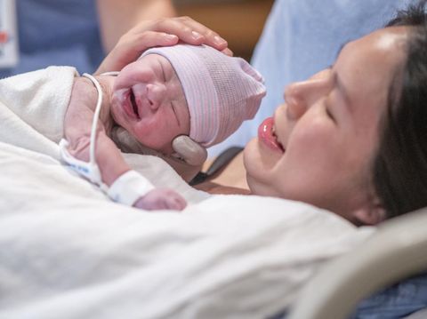 Pregnant young woman lying on the bed in delivery room. Side view of happy pregnant female resting on bed in hospital ward. Healthcare and pregnancy concept