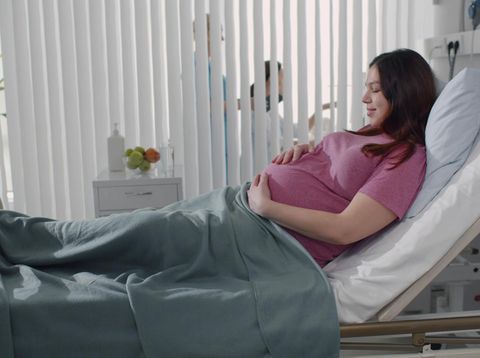 Pregnant young woman lying on the bed in delivery room. Side view of happy pregnant female resting on bed in hospital ward. Healthcare and pregnancy concept