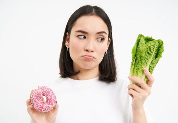 Perempuan sedang memegang donat dan sawi