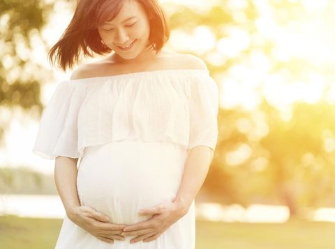 Pregnant woman touching her big belly and walking in the park